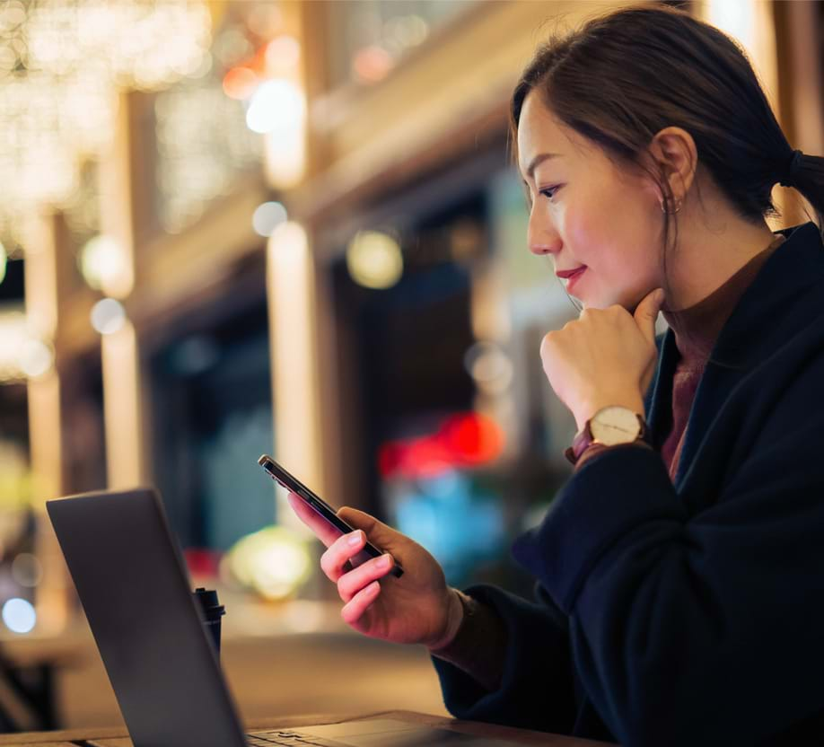 woman looking at phone and laptop