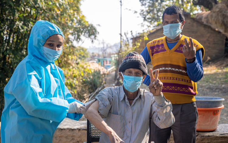 Female Nurse with PPE kit protective mask and gloves preparing a male patient's arm for vaccination in rural village of India. Healthcare workers giving vaccine to a people in pandemic.